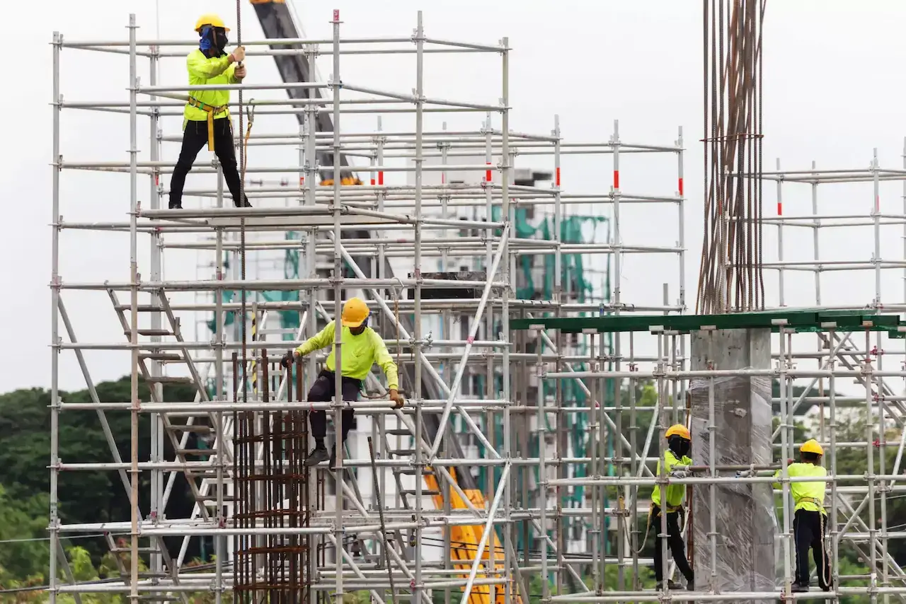 Echipă de schelari asiatici montând schelă pe un șantier de construcții din România.